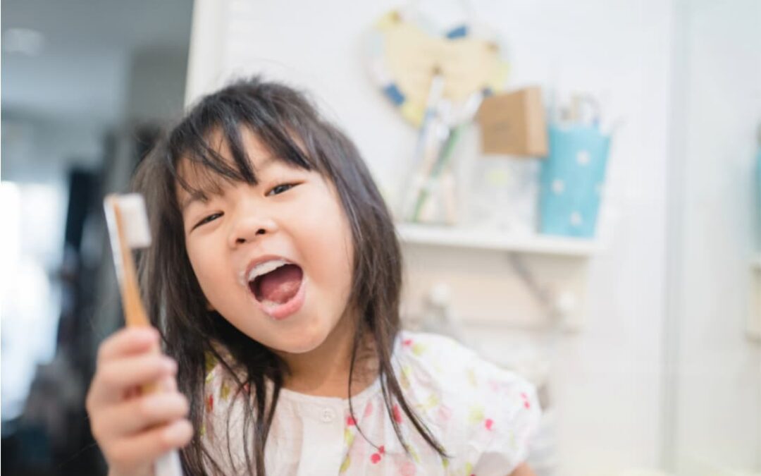 Young child holding a toothbrush in a bathroom, highlighting the importance of replacing children’s toothbrushes regularly as bristles wear faster.