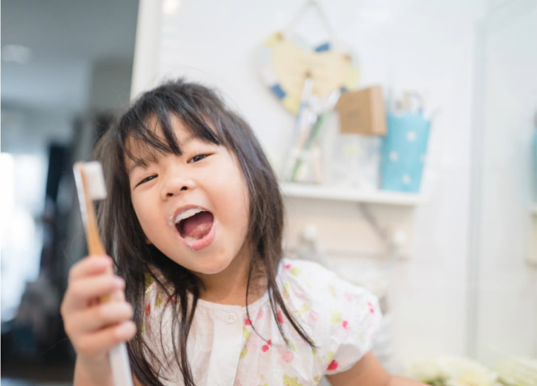 Young child holding a toothbrush in a bathroom, highlighting the importance of replacing children’s toothbrushes regularly as bristles wear faster.