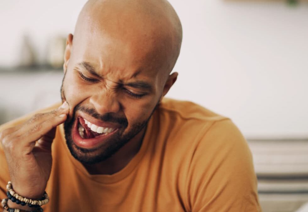 Adult experiencing jaw and tooth pain, illustrating how teeth grinding or clenching can cause tooth sensitivity and facial discomfort.