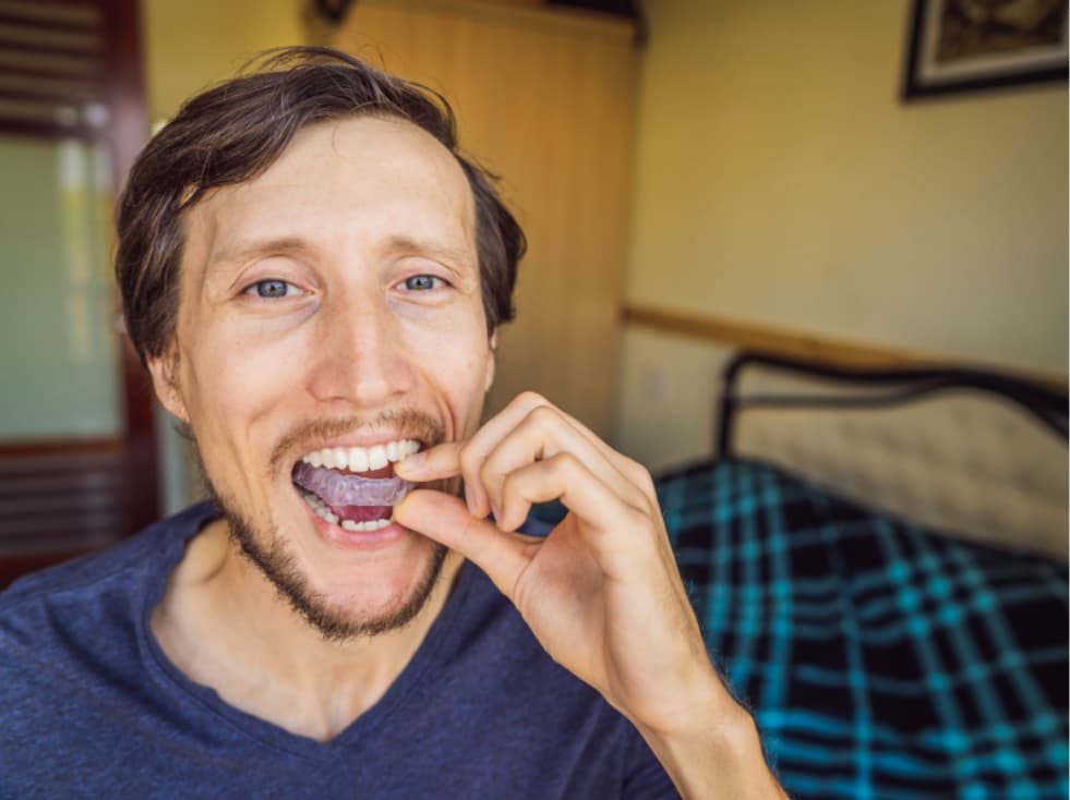 Man placing a custom nightguard onto his teeth, demonstrating how nightguards help protect against grinding.
