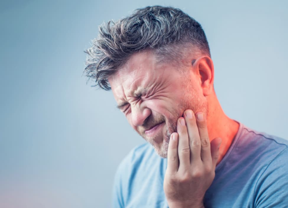 Man grimacing in pain and holding is jaw due to cavity infection
