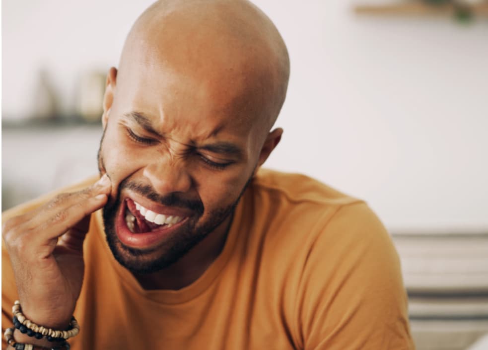 Adult experiencing jaw and tooth pain, illustrating how teeth grinding or clenching can cause tooth sensitivity and facial discomfort.
