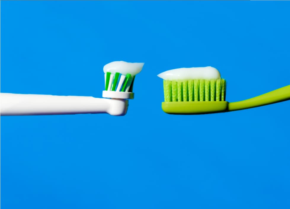 Side-by-side comparison of a manual toothbrush and an electric toothbrush head with toothpaste, illustrating differences in brushing technology.